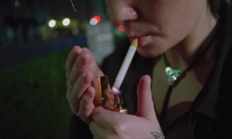 Young female person lighting a cigarette and smoking it on an urban area outdoors during day time