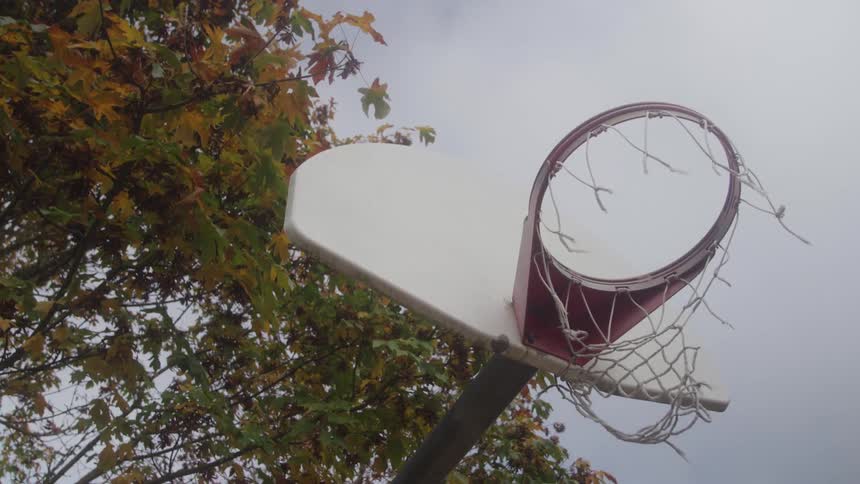 A basketball passes through a basketball hoop with a net