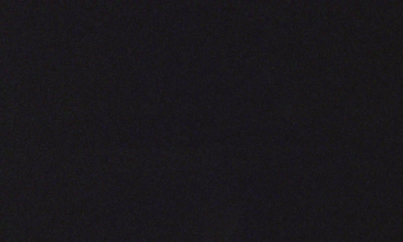 A dark grainy frame with faint neon green light streaks and shots of vehicles across a mostly black background