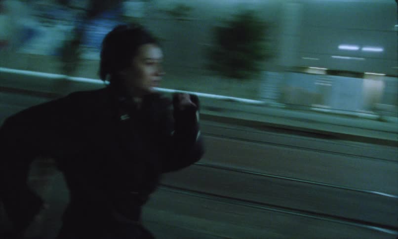 A young woman frantically runs down a city sidewalk at night