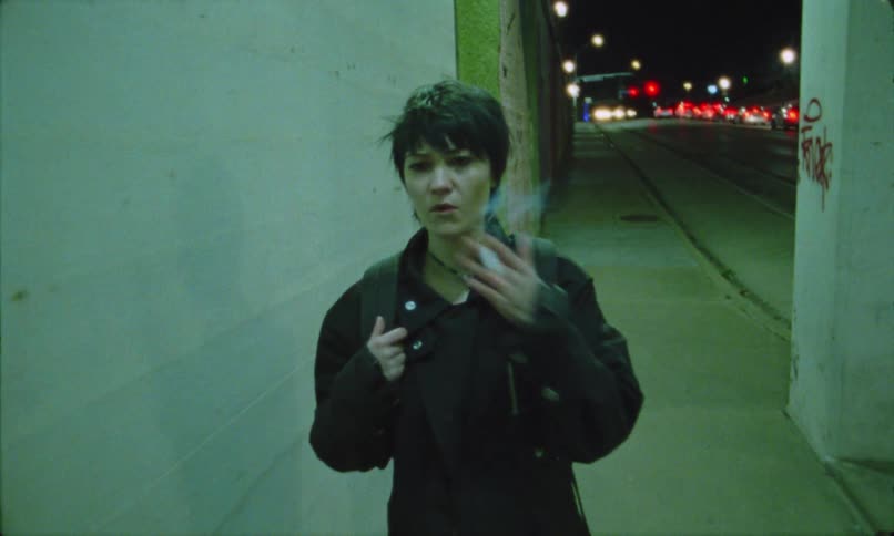 woman with dark hair smoking and walking on a busy street at night
