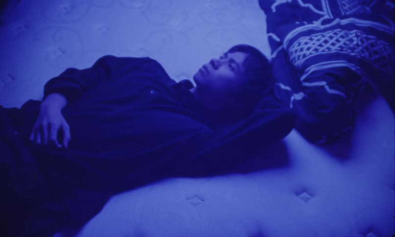 Man lying on a mattress under bluish light