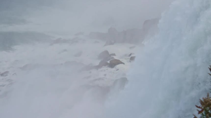 A powerful waterfall plunges over a rocky ledge and the view follows the thundering cascade down into the churning mist and rapids below