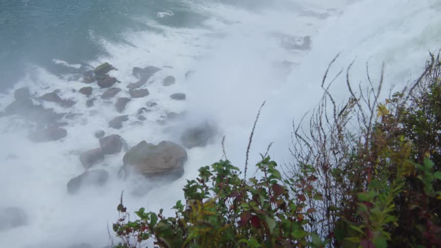 Foaming water flowing down a waterfall encircles the boulders at the base of the cliff on an autumn day