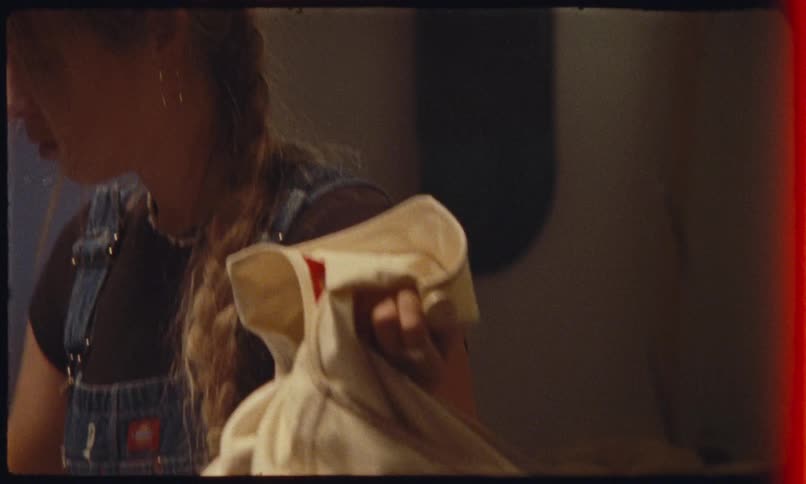 Person wearing denim overalls smooths a piece of clothing on the table