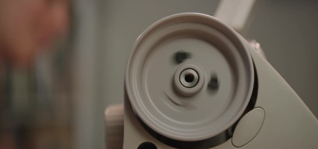 A closeup shot focuses on the white spool pin winding mechanism of a sewing machinea persons hand wearing rings and with red nail polish briefly touches and then engages the wheel causing it to spin rapidly to wind a bobbin
