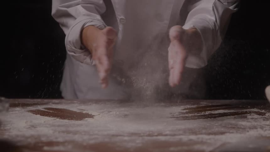 Close up of a baker handling baking flour powder on a table top