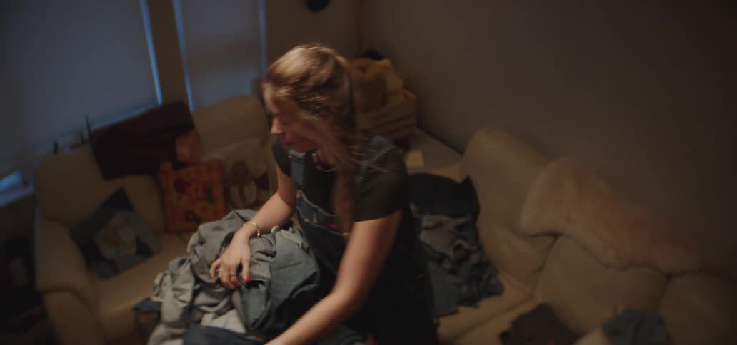 Young woman standing up on a living room sorting a pile of clothes indoors during day time