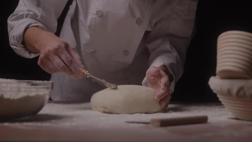 The chef uses a utensil on the dough