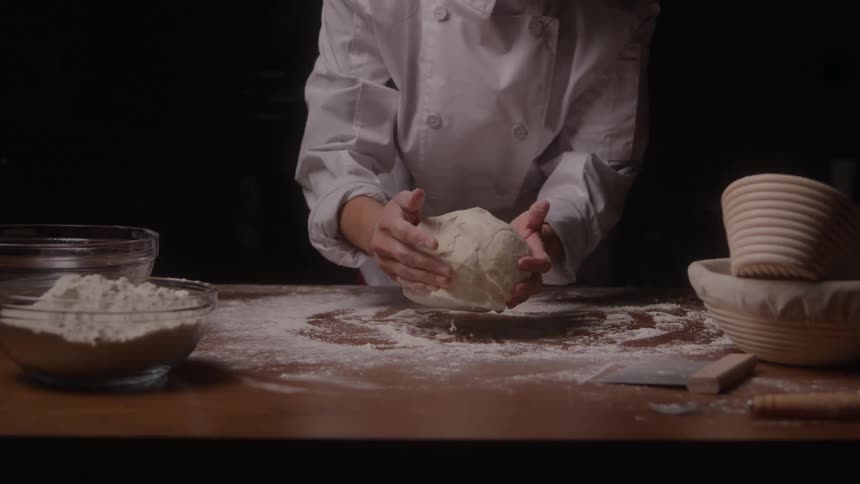 A baker kneads dough on a floured table under warm light
