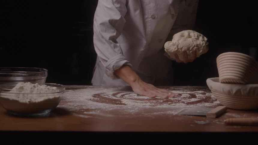The woman is kneading dough and covering it with flour
