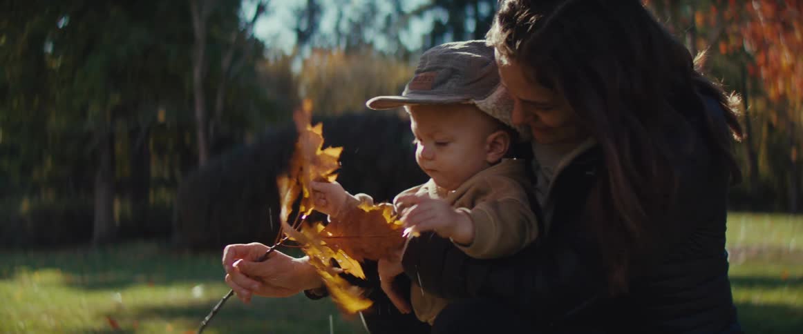 A mother and her young son play with autumn leaves together in a sunny park