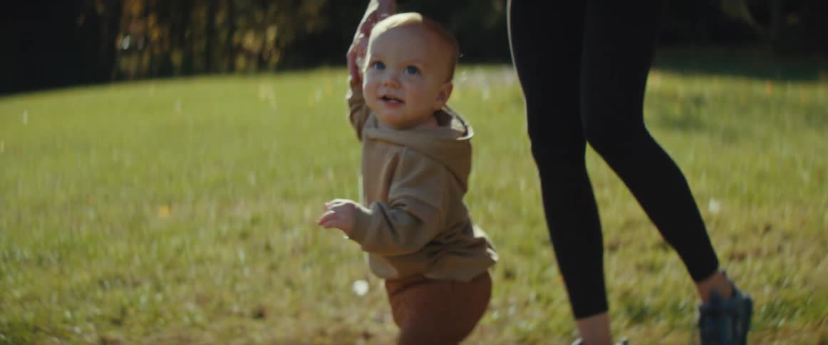 A very small child struggles to walk with the help of a woman