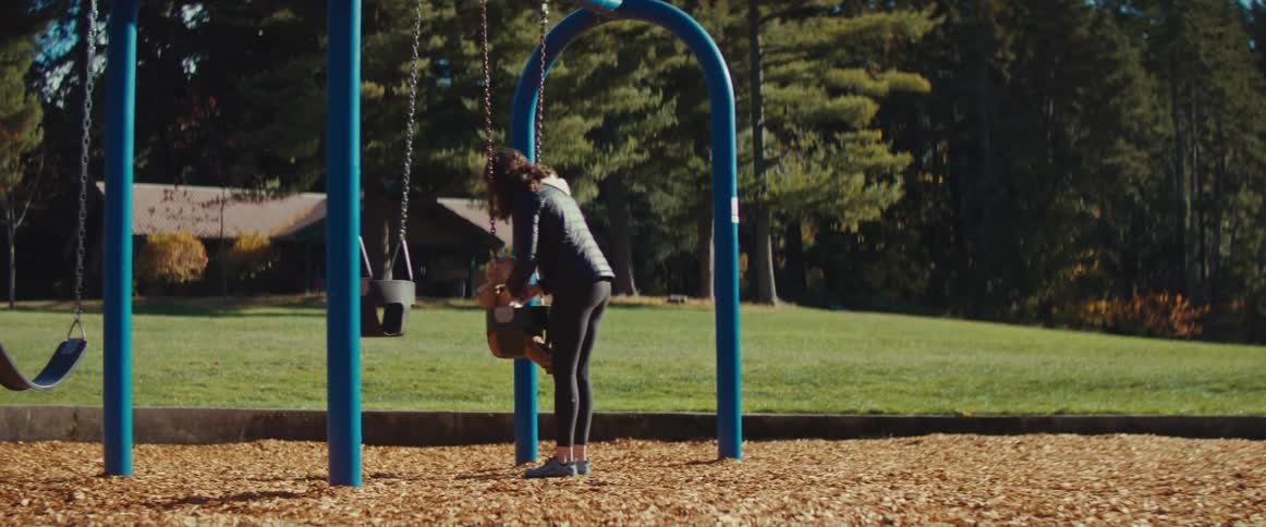 Mother places her baby in a park swing to play during daytime