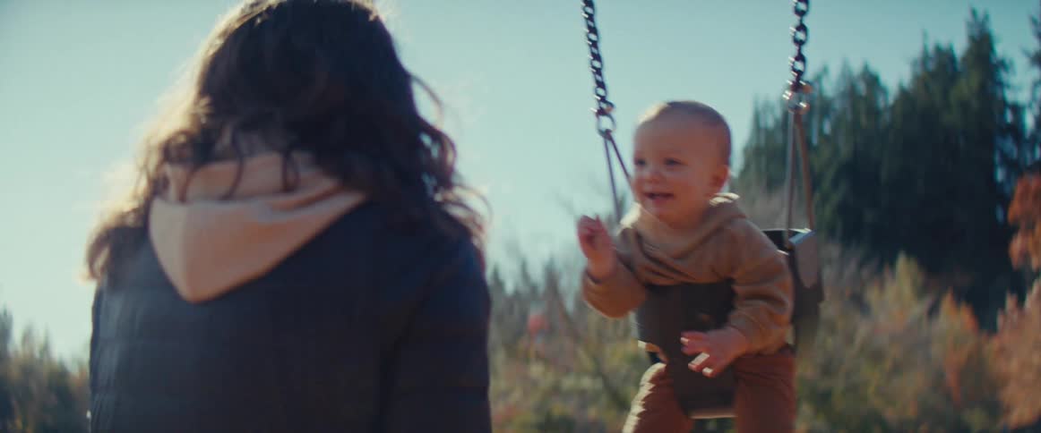 Mother playing with her baby at a swing in an outdoor play area during daytime
