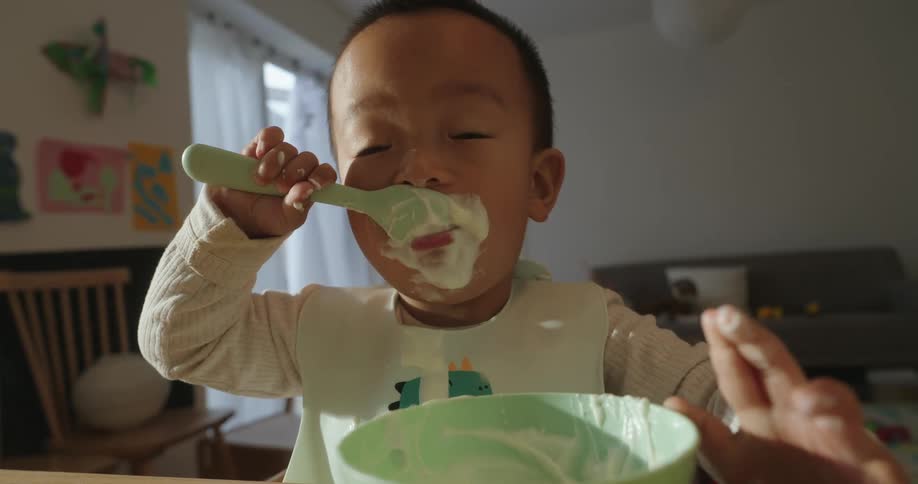 A child eating with a spoon from a bowl while the mother adjusts the plate at midday