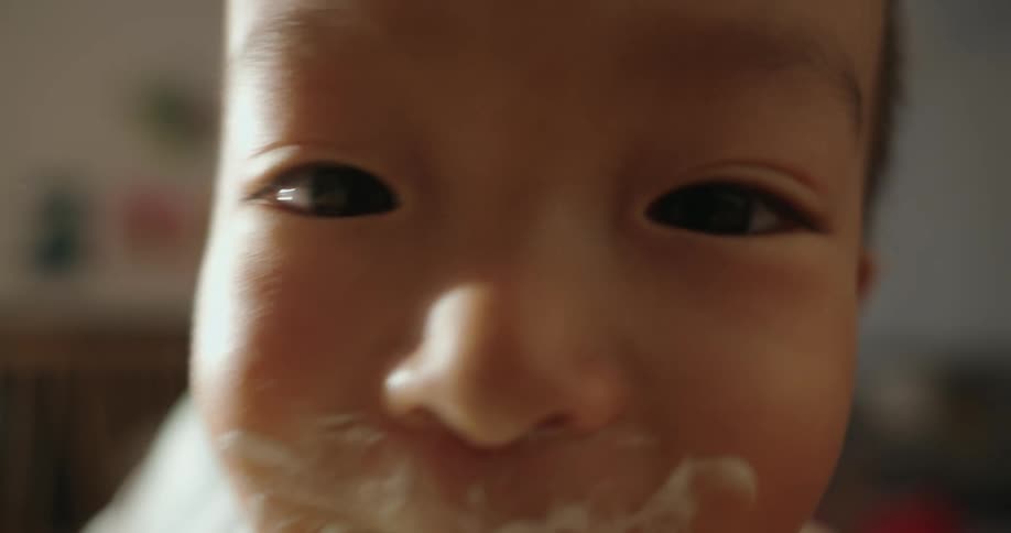 A toddler with food stains around his mouth sits at the dining table after a meal at midday