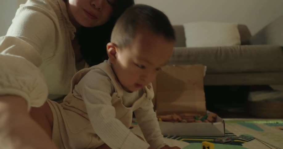 A mother and her young son playing on a play mat in the living room with a toy car
