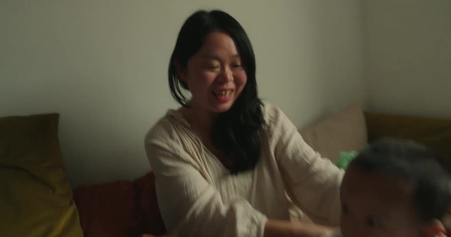 A mother and father play and laugh with their young son in a cozy bedroom