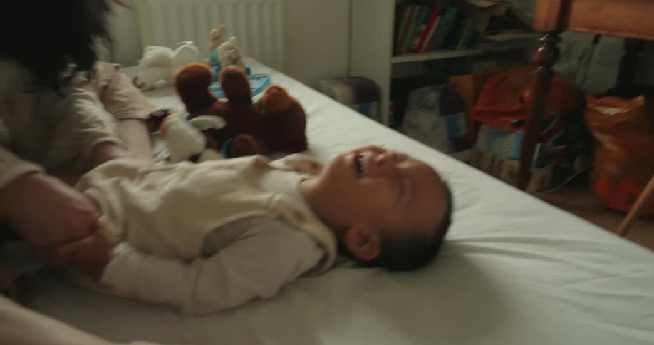 A mother and her son play and laugh together on a bed in a cozy bedroom