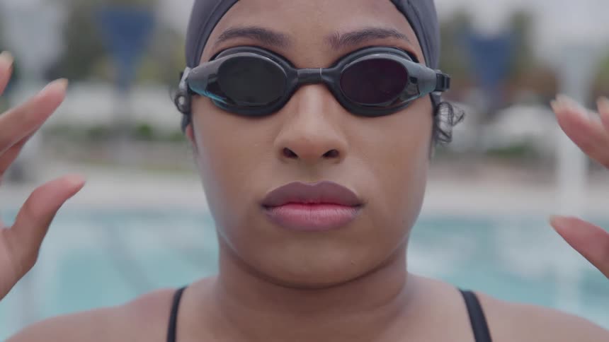 The face of a woman putting on black swimming goggles and she is wearing a swim cap