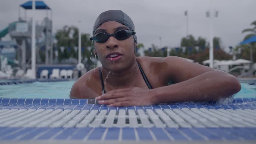 A young black woman swimming in an outdoor pool during daytime