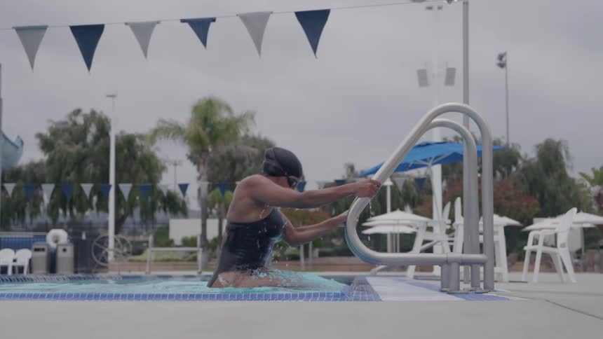 A young woman in a swimsuit steps out of an outdoor pool after swimming