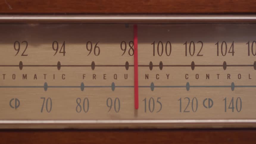 An analog radio receiver being tuned with a red indicator stick moving to the left