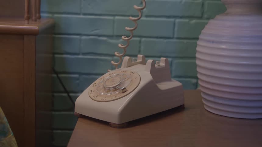 Persons hand lifts the receiver from an old rotary phone on a table and hangs it up