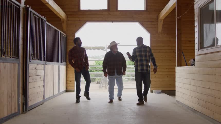 Three farmers talk while walking inside a barn on a farm