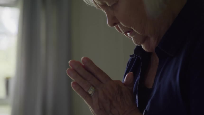 A woman is sitting in a room and praying with her hands together