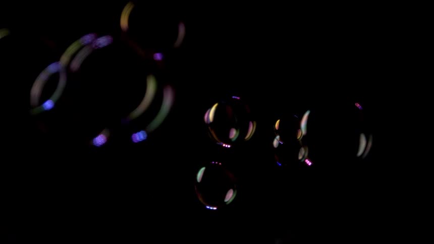 Several soap bubbles of different colors floating above a black background