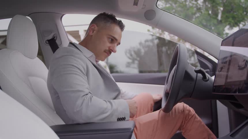 Man gets in his car and sits down in the drivers seat as he holds the steering wheel