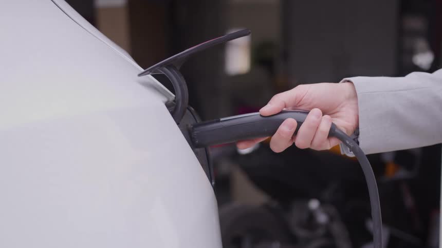 Person plugs a cord into the charging port of an electric vehicle