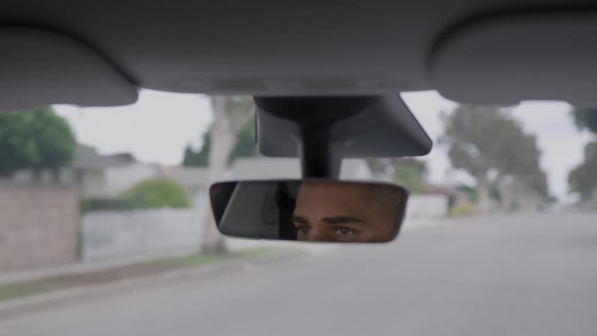 A rear view mirror showing the eyes of a man as he drives a car on a suburban road