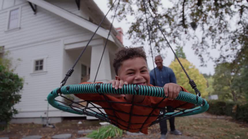 Joyful parents push their child on a swing in the backyard