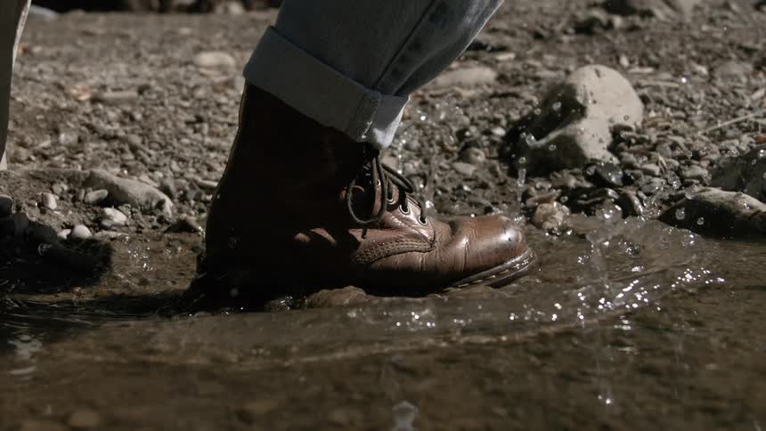 Close up of a person stepping into a water puddle with their boots while walking outdoors during daytime