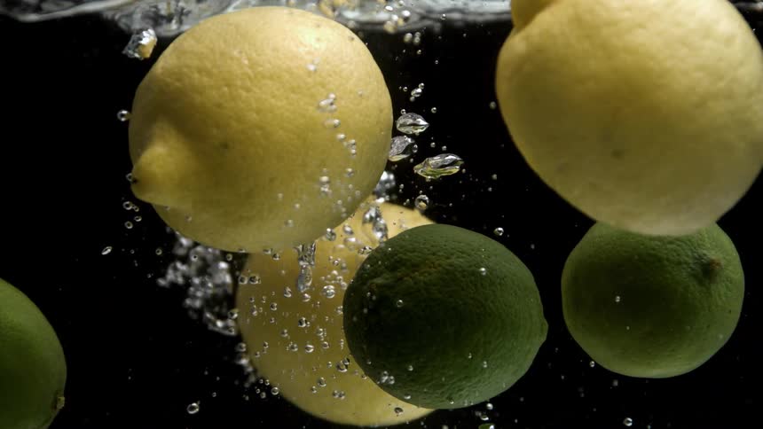 Lemons and limes submerged create bubbles and splashes as they fall into the water