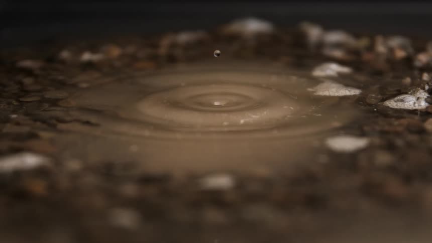 A drop of water splashes into a muddy puddle creating ripples