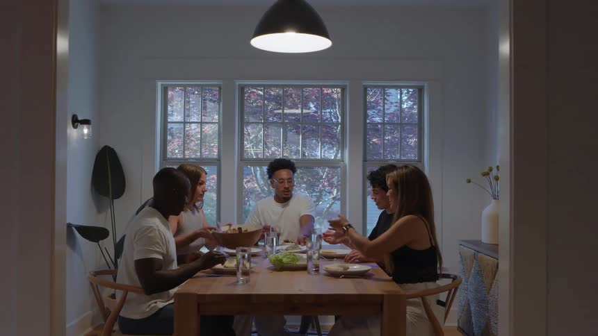 A group of friends including two women and three young men having dinner together at the dining table