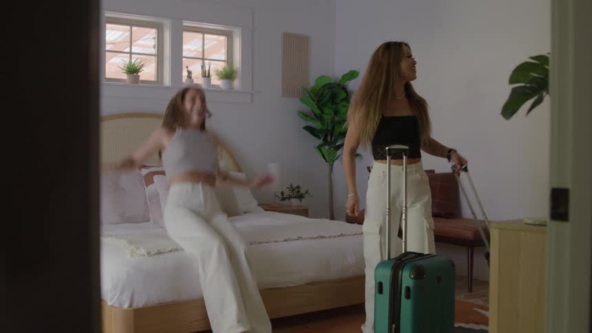 The two women roll there luggage and then jump into the bed