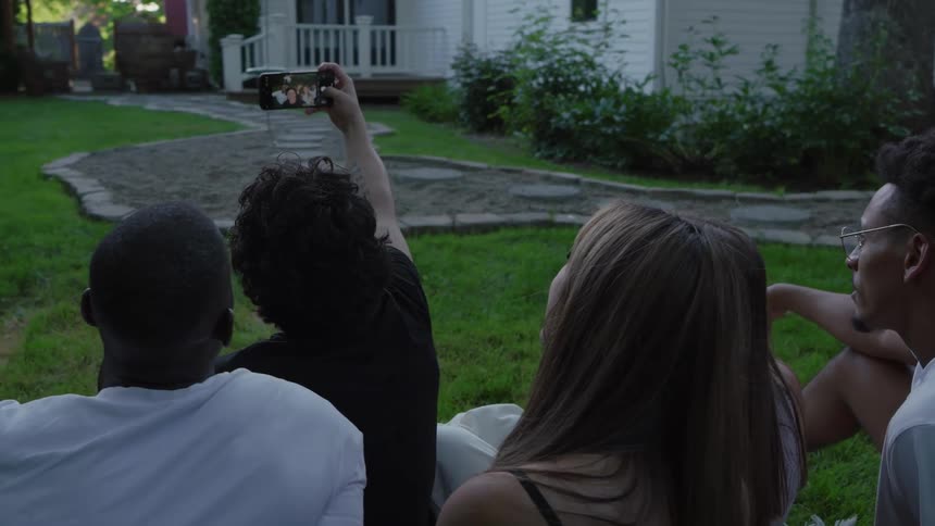 Group of friends sitting on the lawn take a selfie in front of the house