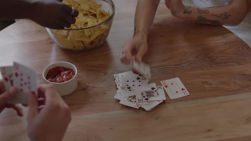 Hands play cards while snacks sit on the table