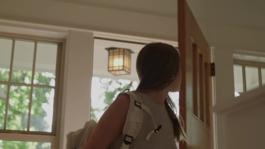 Young woman returns home through the front door and looks around on a summer day