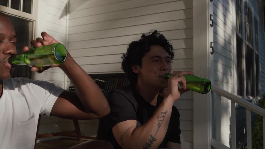 Two young men sit on the front porch drinking beer