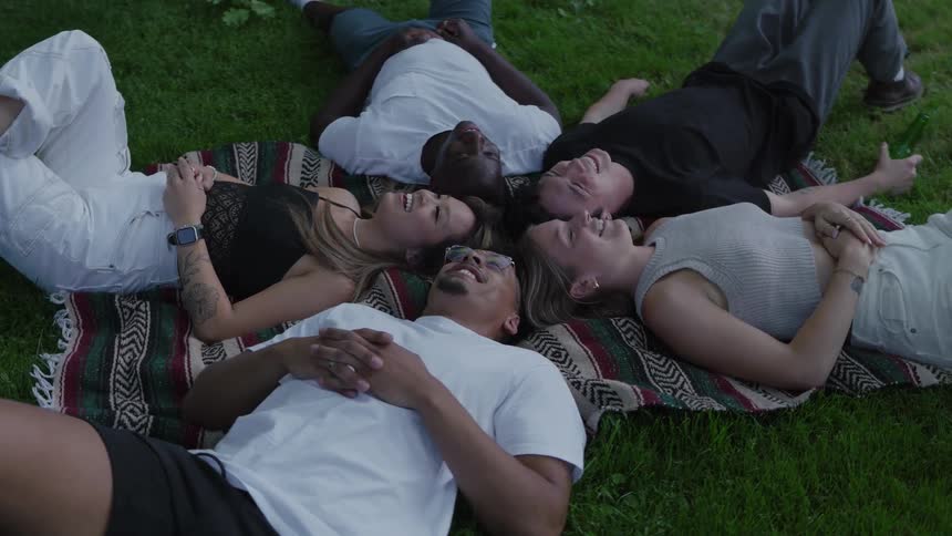 Friends lying in a circle on the grass laugh together at night