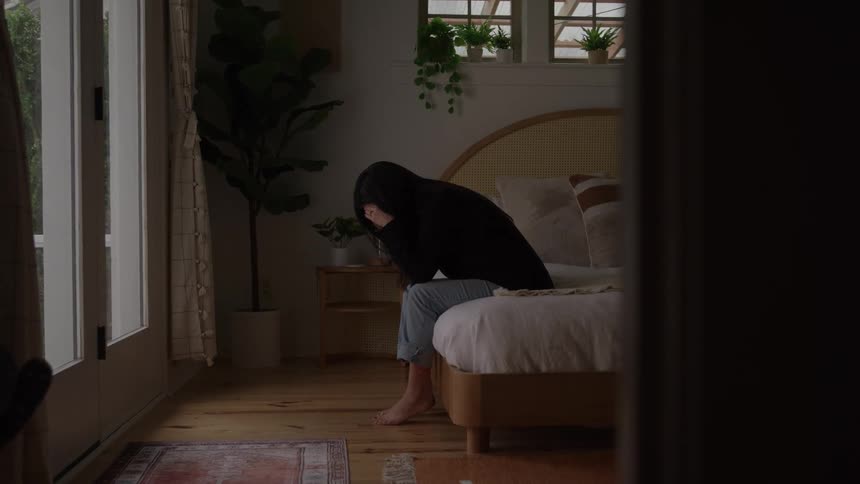 Woman sitting on the edge of the bed with her hands covering her face