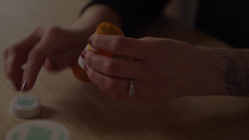 A persons hand picking up an orange bottle of medicine taking out a pill and placing it in their hand