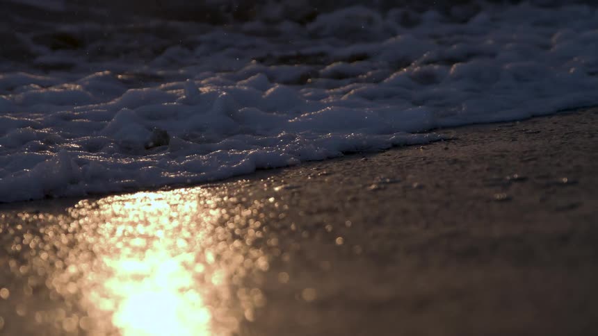 Sunlight shines on the coast as waves roll into shore and over the beach
