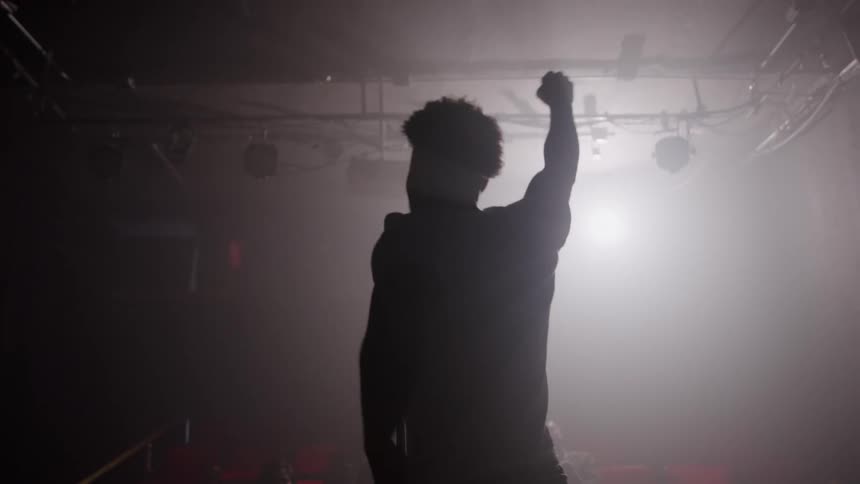 Man raising alternate fists on a stage is silhouetted by a spotlight